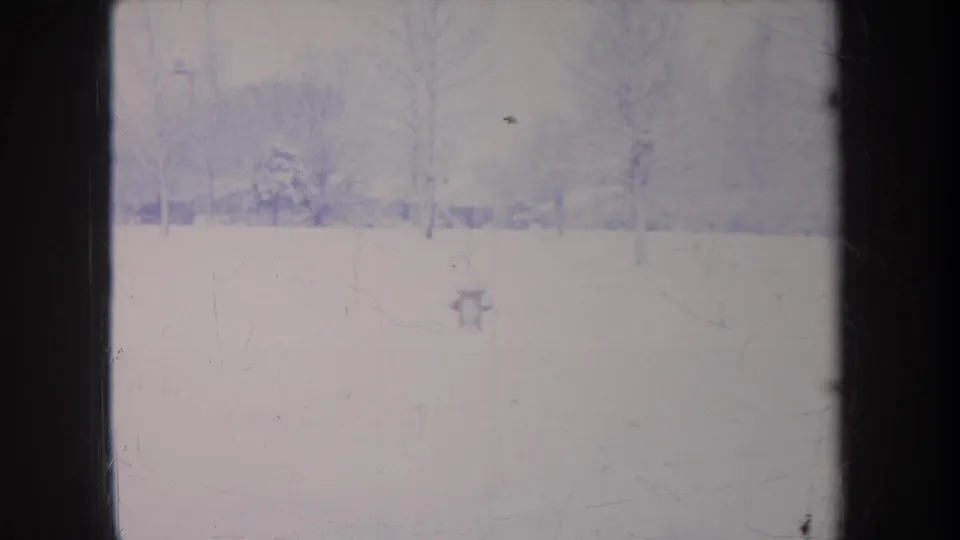 Faded 1968 Michigan 8mm frame showing snow-covered ground, bare trees, and distant structures softened by haze and film texture.
