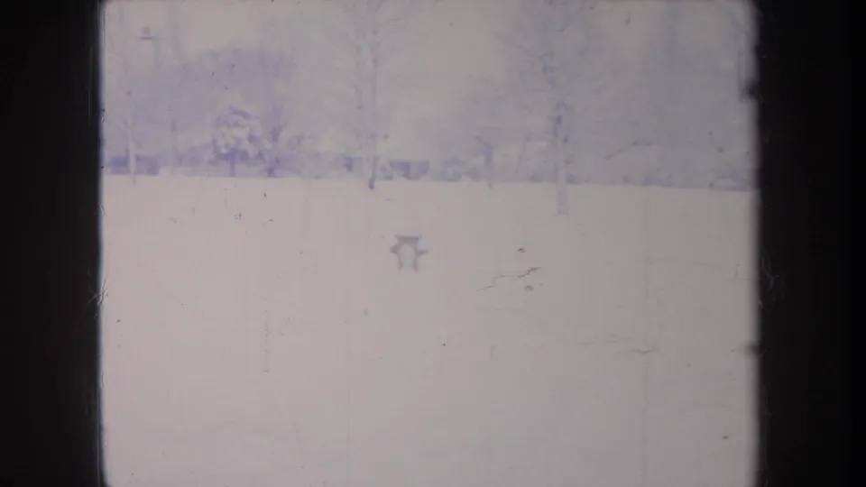 1968 Michigan home-movie frame showing a quiet snowy field, distant tree line, and leafless trees in soft 8mm color.