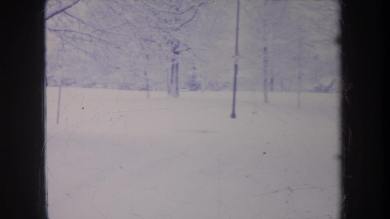 1968 Michigan winter home-movie frame with bare trees over a snowfield, faded color, and visible 8mm film borders.