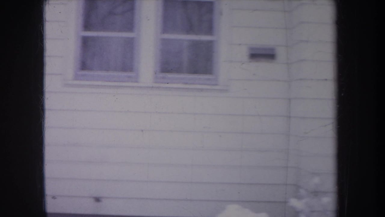 1968 Michigan home-movie view of white siding with paired windows and a small exterior fixture or mailbox.