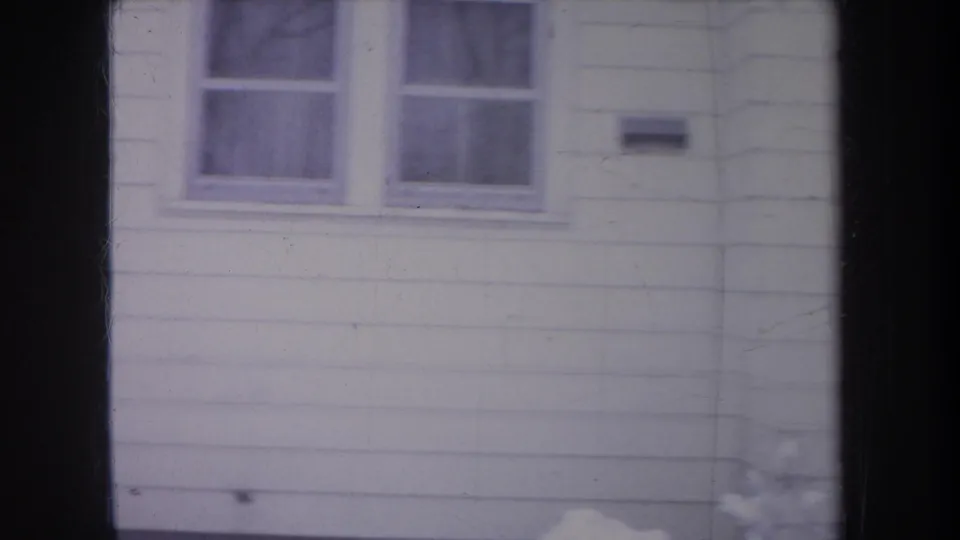 1968 Michigan home-movie view of white siding with paired windows and a small exterior fixture or mailbox.