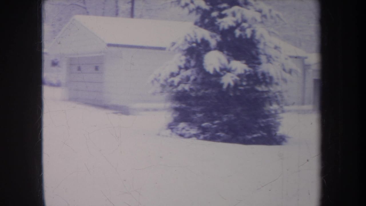1968 Michigan 8mm frame showing a snow-covered yard, garage-like building, shrubs, and bare winter branches.