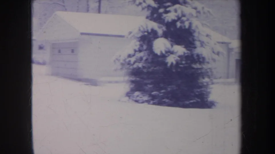 1968 Michigan 8mm frame showing a snow-covered yard, garage-like building, shrubs, and bare winter branches.