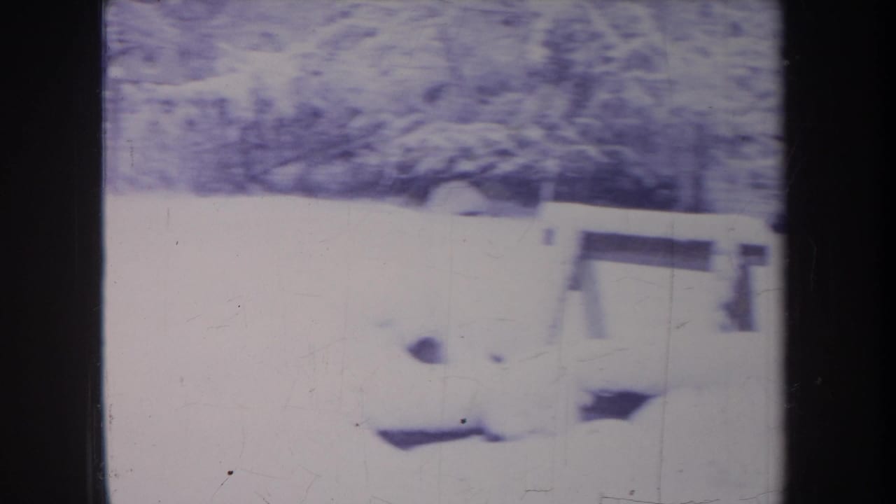 Snow-covered backyard with a low fence or railing and winter brush in faded Michigan 1968 8mm footage.