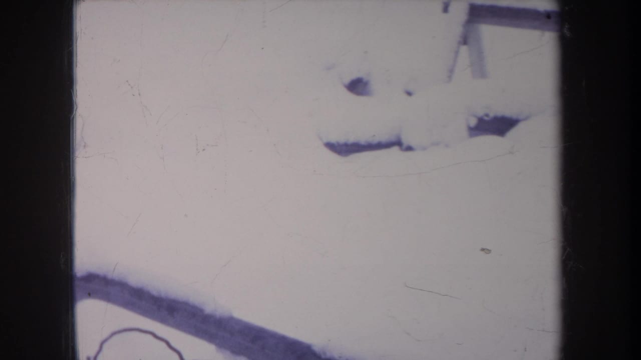 1968 Michigan 8mm frame showing deep backyard snow, a partial bench edge, and the dog partly obscured near the bottom of the frame.