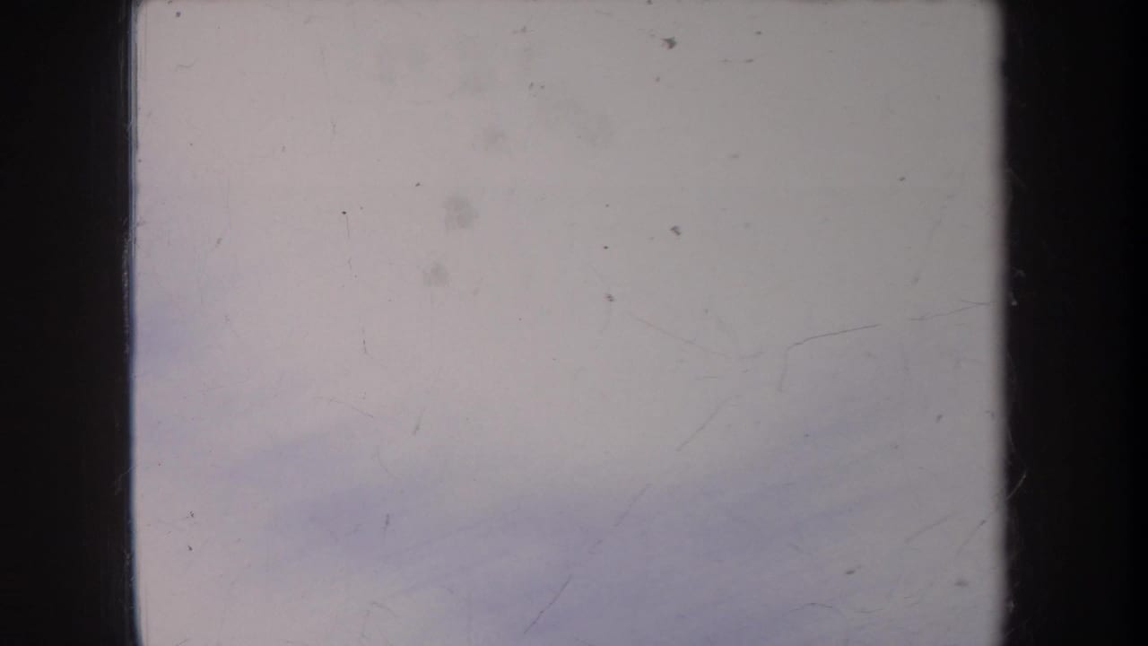 Pale 8mm frame from the Michigan winter clip showing mostly snow or bright exterior surface with scratches, dust, and dark gate edges.