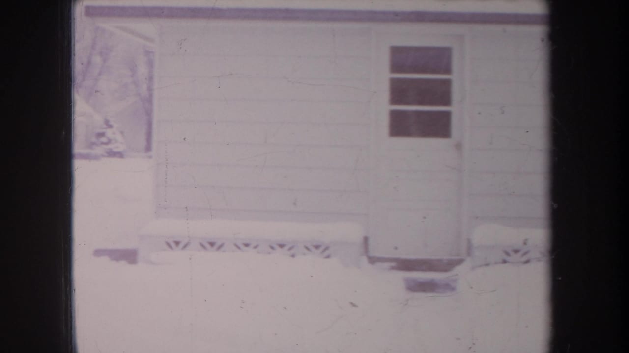 1968 Michigan 8mm frame showing a snow-covered house or garage exterior, small window, roofline, and visible film scratches.