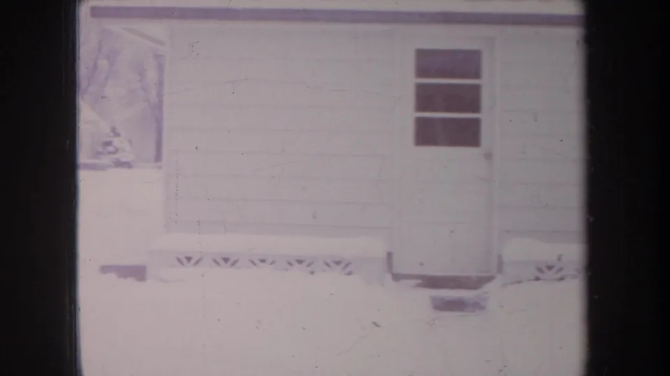 1968 Michigan 8mm frame showing a snow-covered house or garage exterior, small window, roofline, and visible film scratches.