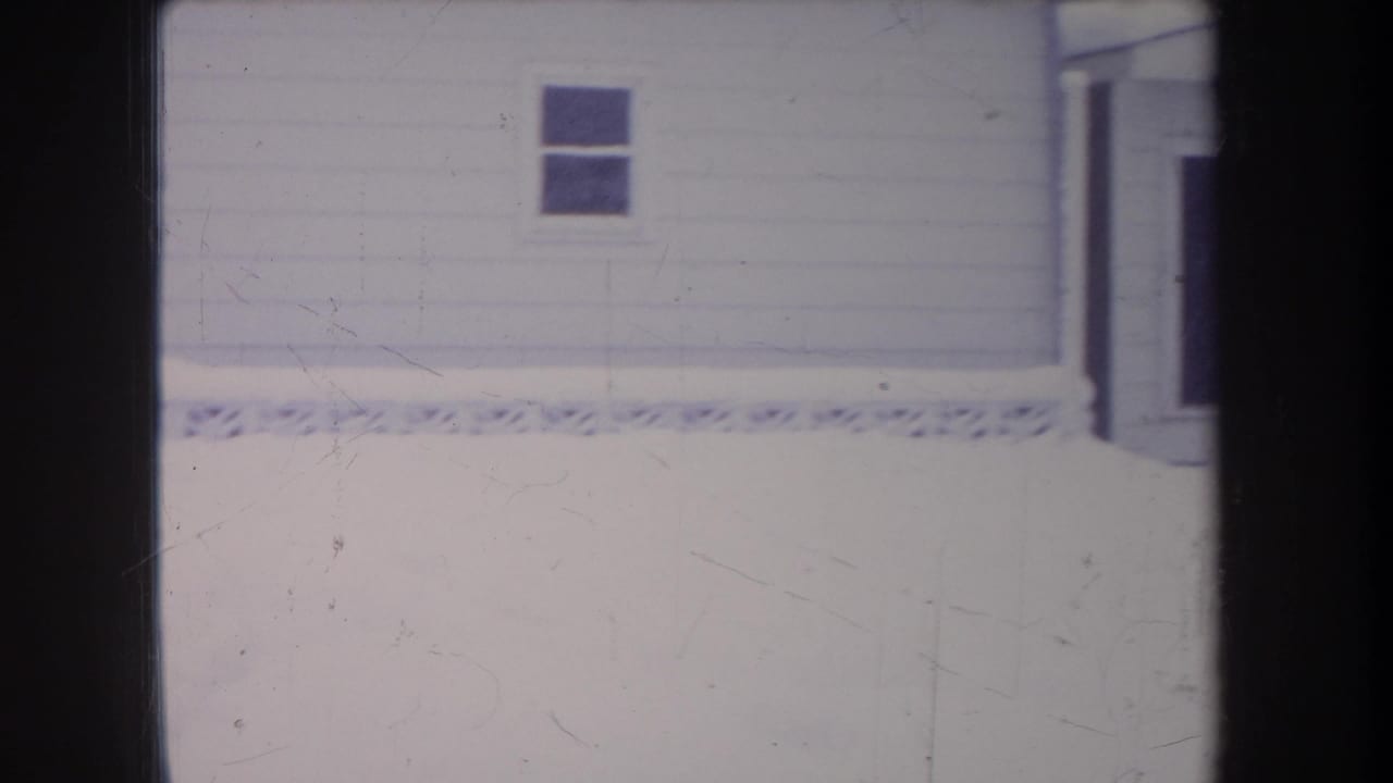 White house wall with two windows above a bright snowy yard.