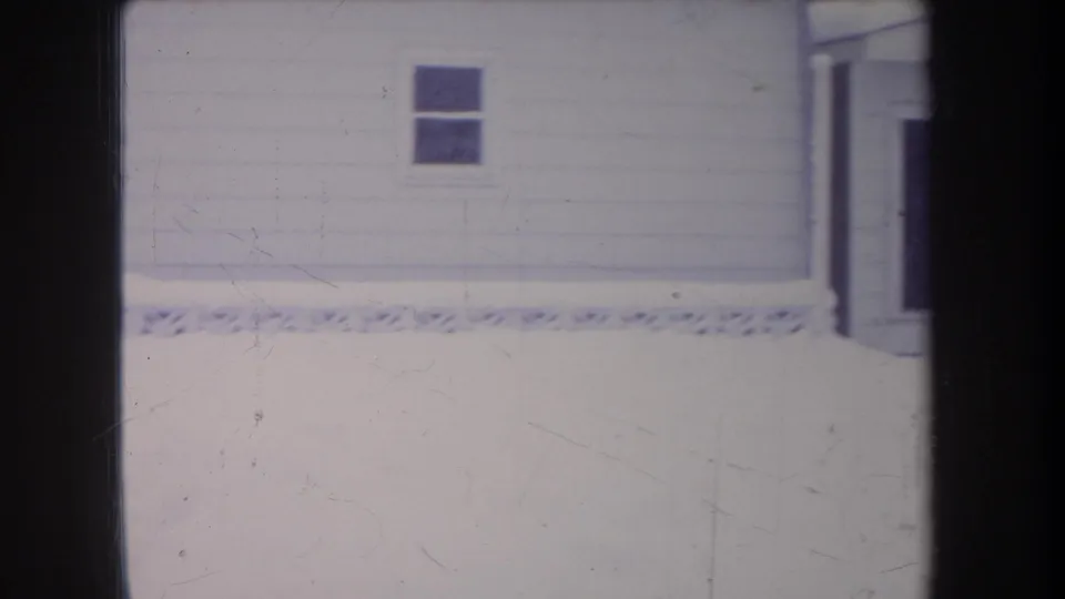 1968 Michigan residential exterior with a white wall, two dark windows, and overexposed snow in the foreground.
