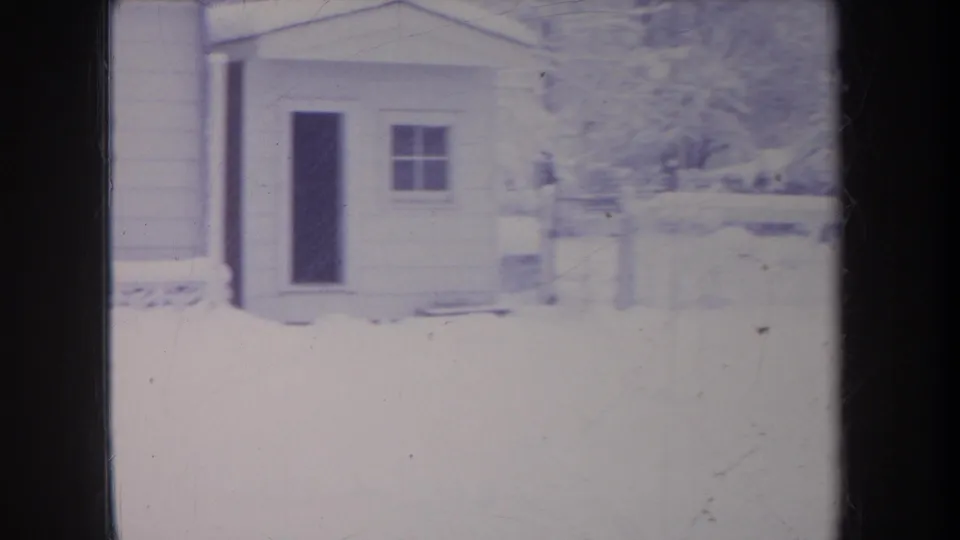 1968 Michigan home-movie frame showing a small outbuilding or side structure with a dark doorway, window, and snow-covered ground.