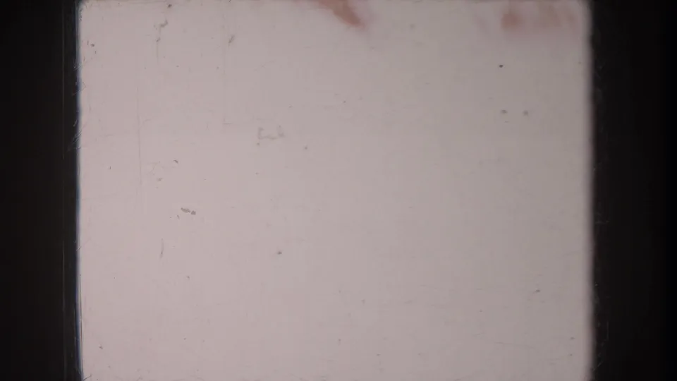 Pale exposed 8mm frame with dark film borders, dust, scratches, and minimal visible scene detail.