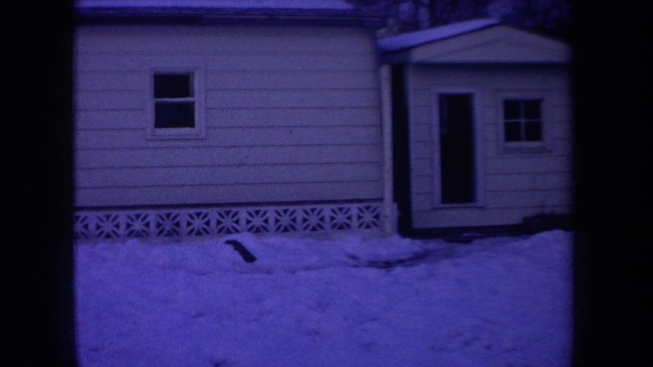 1968 Michigan home-movie frame showing a purple-blue snowy house exterior with siding, window, door, entry structure, and frame edge.