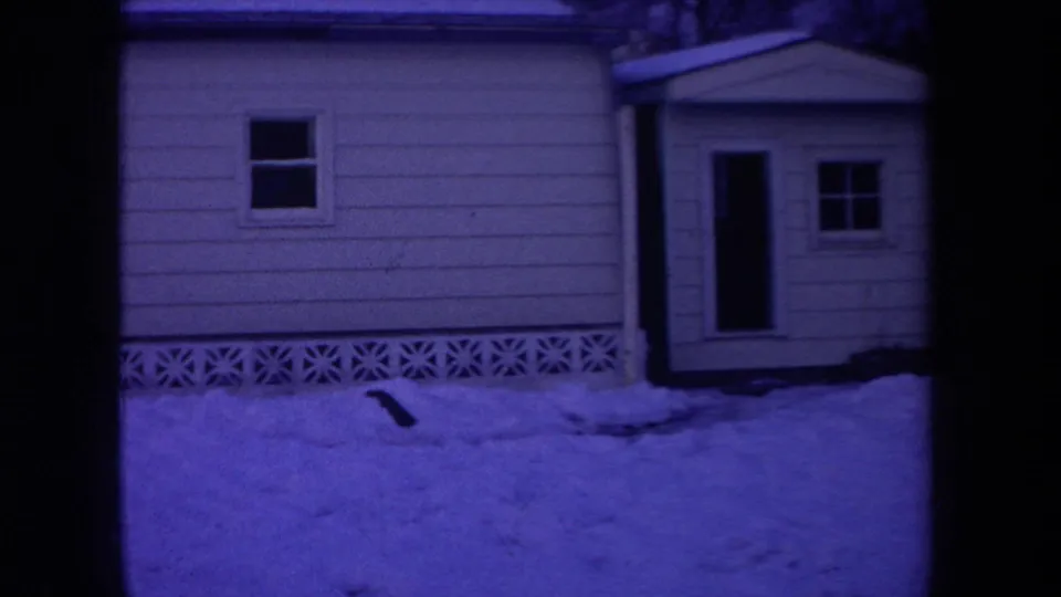 1968 Michigan home-movie frame showing a purple-blue snowy house exterior with siding, window, door, entry structure, and frame edge.