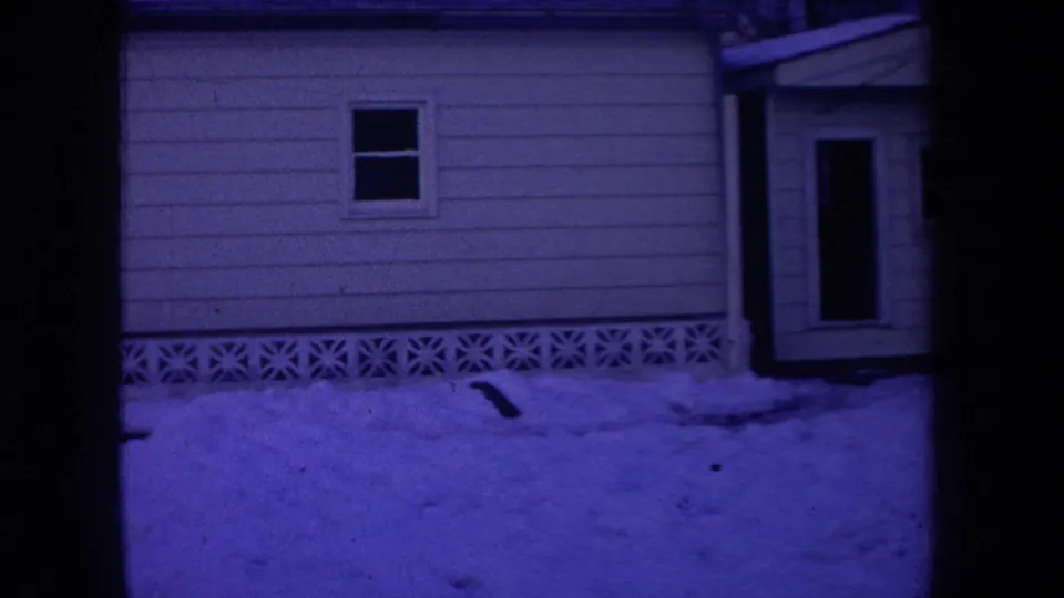 1968 Michigan 8mm frame showing a light-sided house, dark doorway, decorative foundation blocks, and snow-covered ground at night.