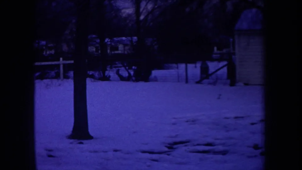 1968 Michigan 8mm frame showing a snow-covered yard with bare trees, a white fence, and neighboring houses in blue night light.