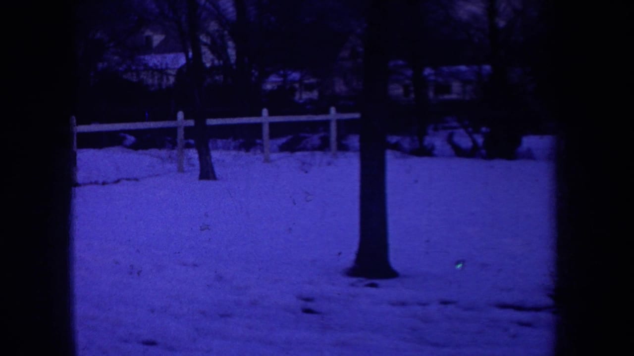 1968 Michigan 8mm frame showing a snow-covered residential yard, bare tree trunk, white fence, and background houses at night.
