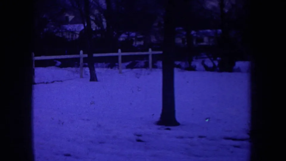 1968 Michigan 8mm frame showing a snow-covered residential yard, bare tree trunk, white fence, and background houses at night.