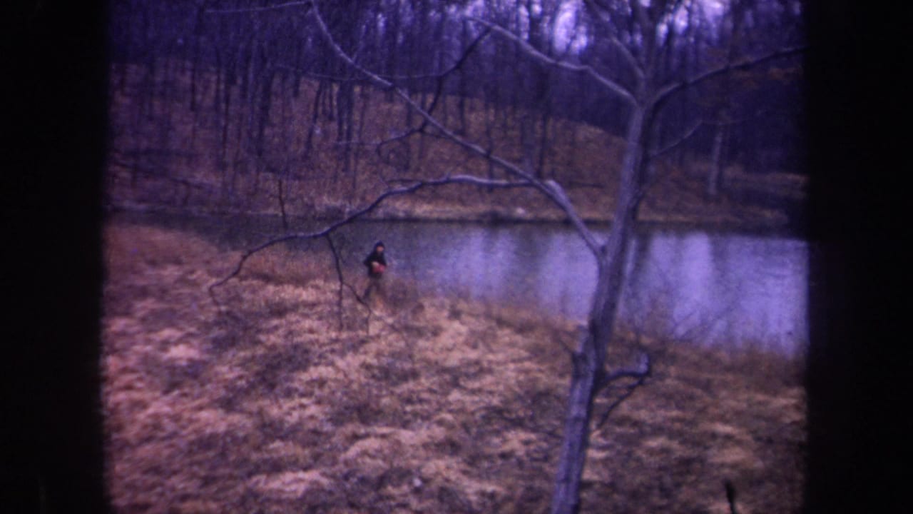 Man in dark clothing runs along the pond bank carrying a red object.
