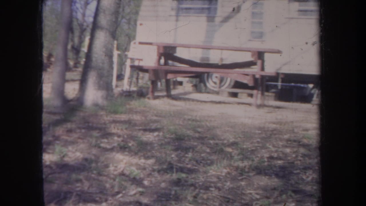 Trailer and picnic table beside trees in a campsite clearing.