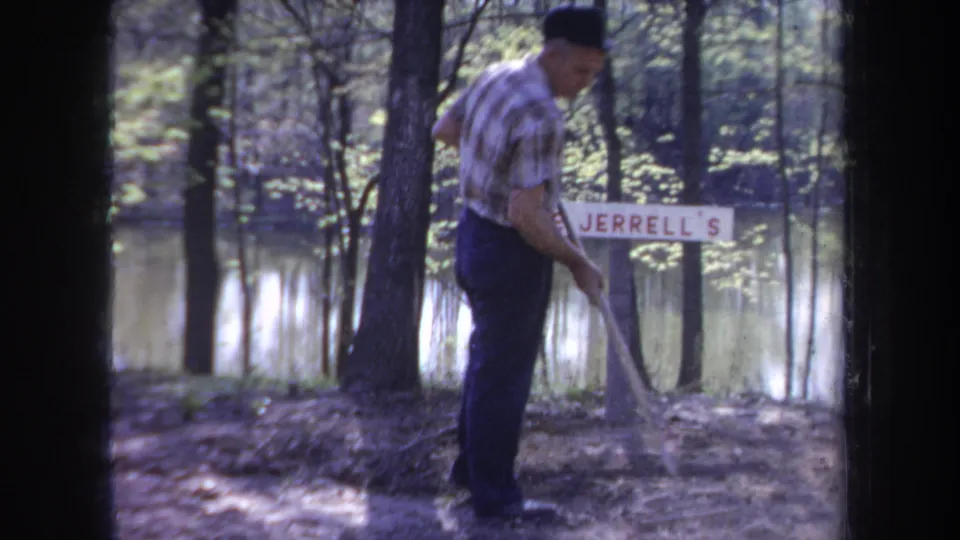 Adult man in plaid shirt and dark trousers appears to clear debris near a Jerrell's sign beside reflective water in Michigan.