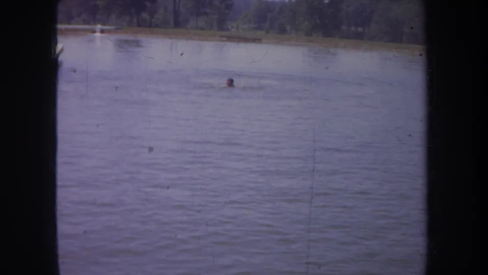 1968 Michigan 8mm frame with a swimmer's head above the water and a wooded shoreline in the background.