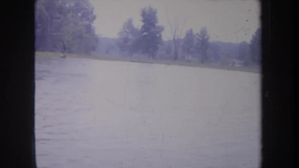 1968 Michigan frame showing open rippled water with distant trees and shoreline, divided by the dark window frame in the foreground.