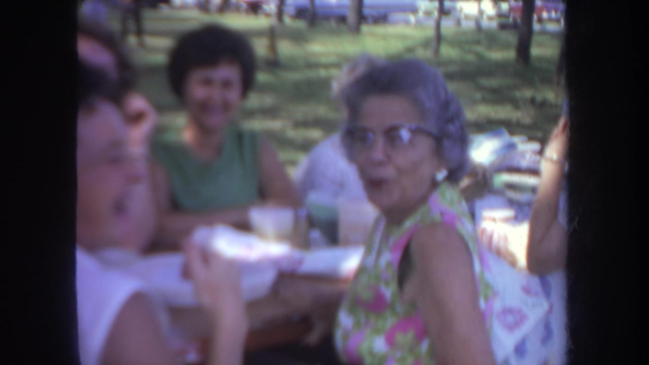 Women sit at an outdoor picnic table in a shaded park.