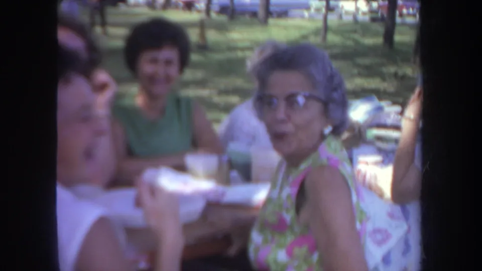 Adult women sit and talk at a picnic table in a Michigan park, with 1960s clothing and soft 8mm home-movie color.