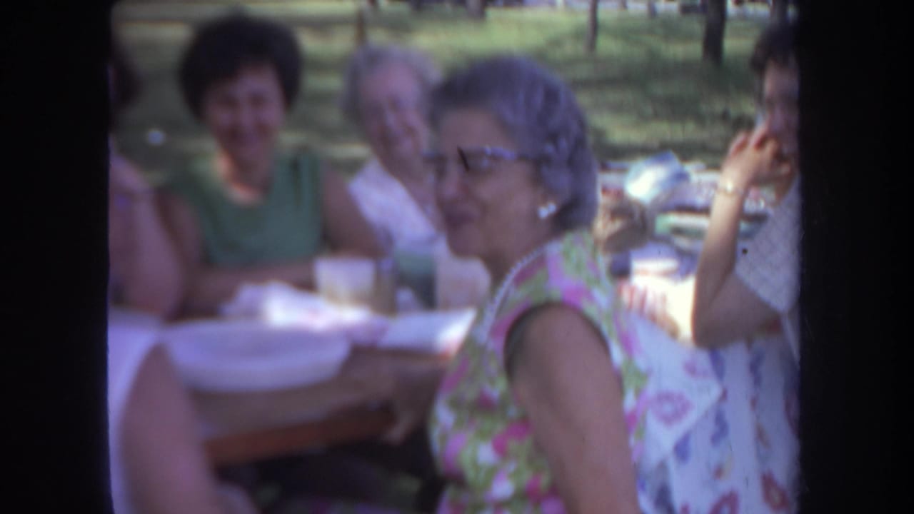 A woman in glasses turns beside a picnic table with others behind her.