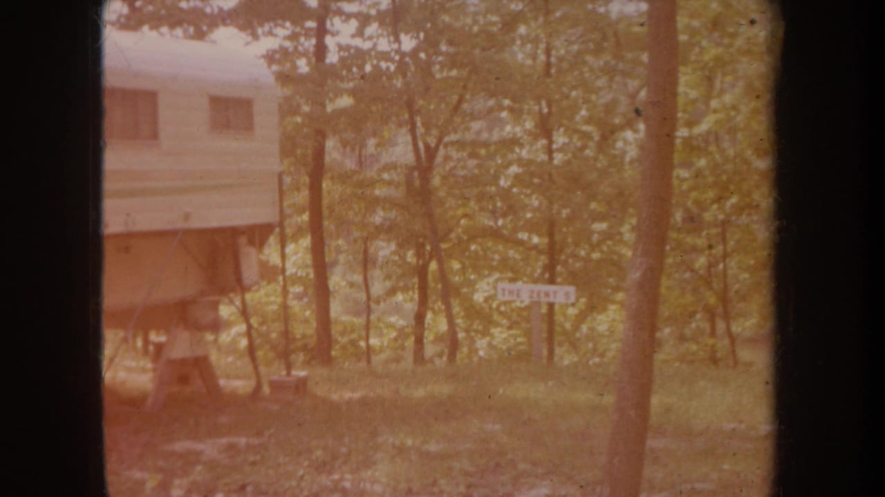 Camper trailer and small sign seen through trees with warm color fading.