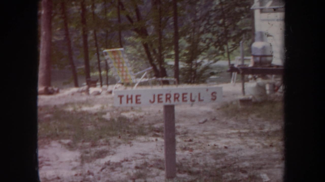 1968 Michigan campsite frame with a painted THE JERRELL'S sign, folding chair, small table, and camper edge in view.