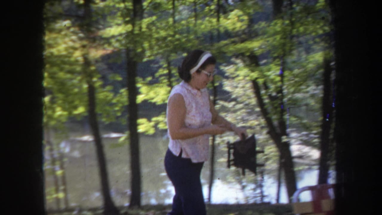 A woman in a sleeveless top stands near the wooded lakeside in Michigan, with water and trees behind her.