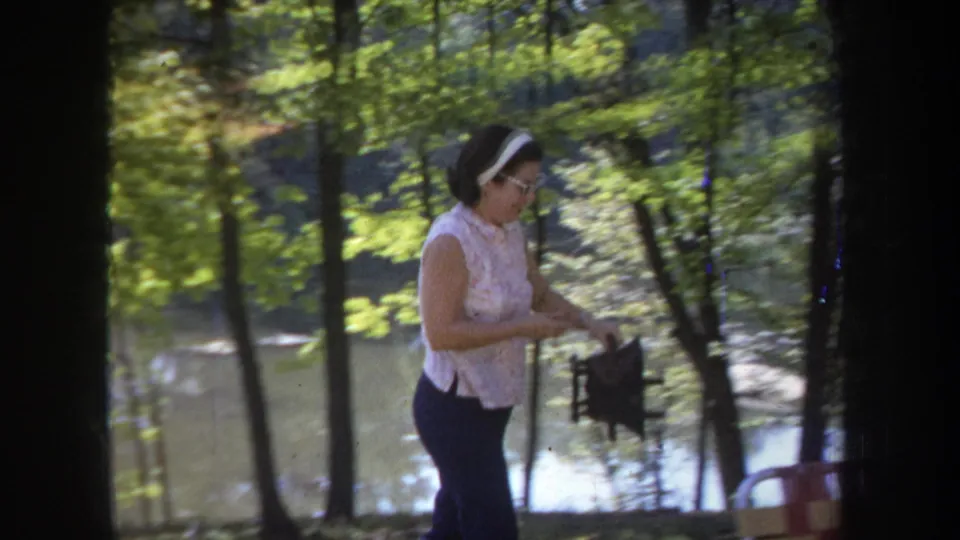 A woman in a sleeveless top stands near the wooded lakeside in Michigan, with water and trees behind her.