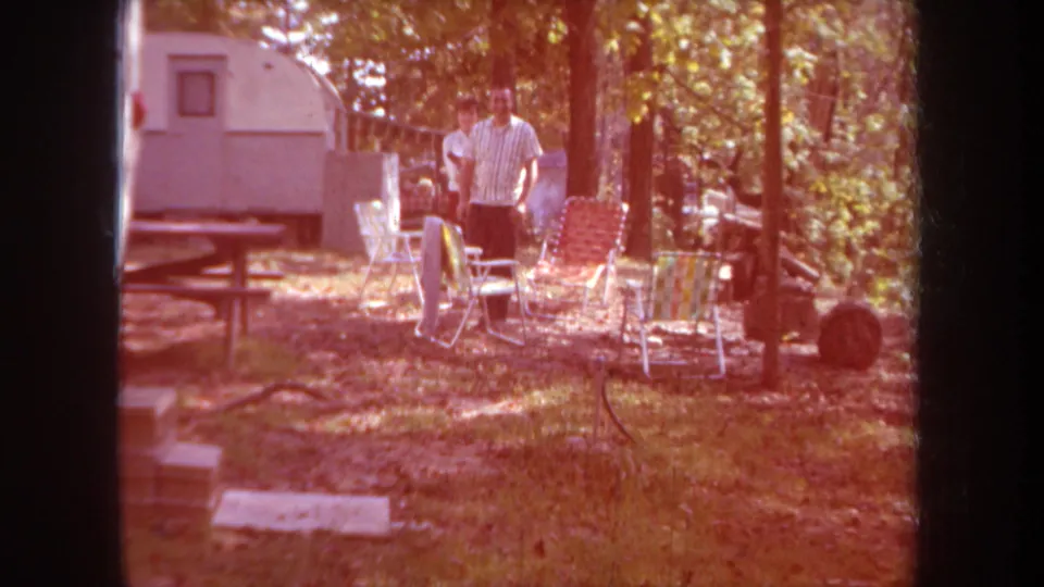 The adults appear among folding lawn chairs beside a white camper trailer, with warm color shift and dark 8mm frame edges.