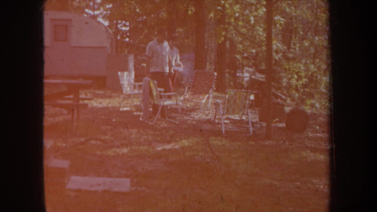 At the end of the clip, the couple remains near folding chairs and a camper trailer as reddish exposure washes over the 8mm frame.