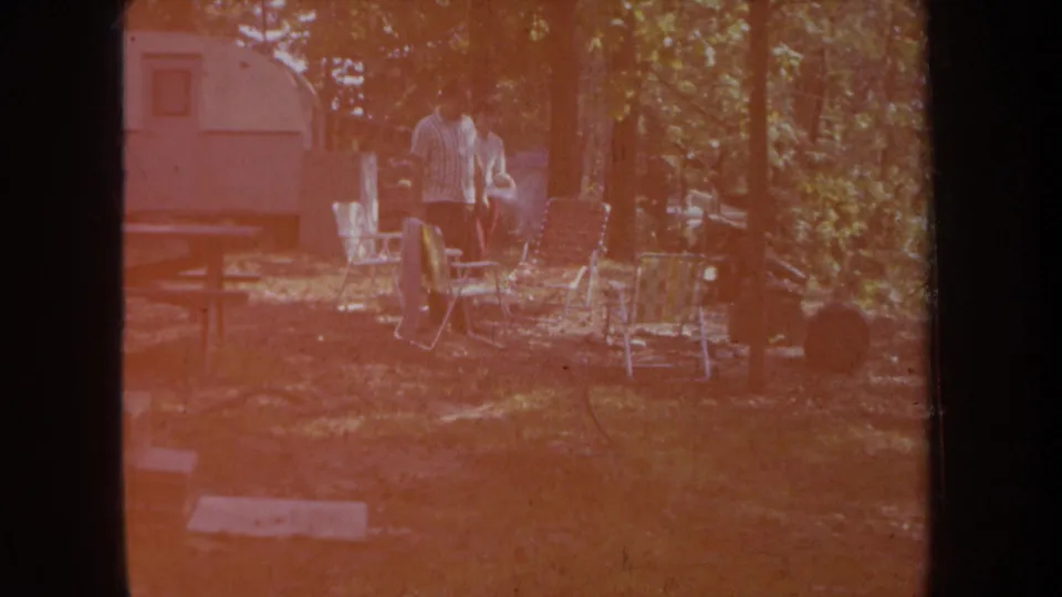 At the end of the clip, the couple remains near folding chairs and a camper trailer as reddish exposure washes over the 8mm frame.