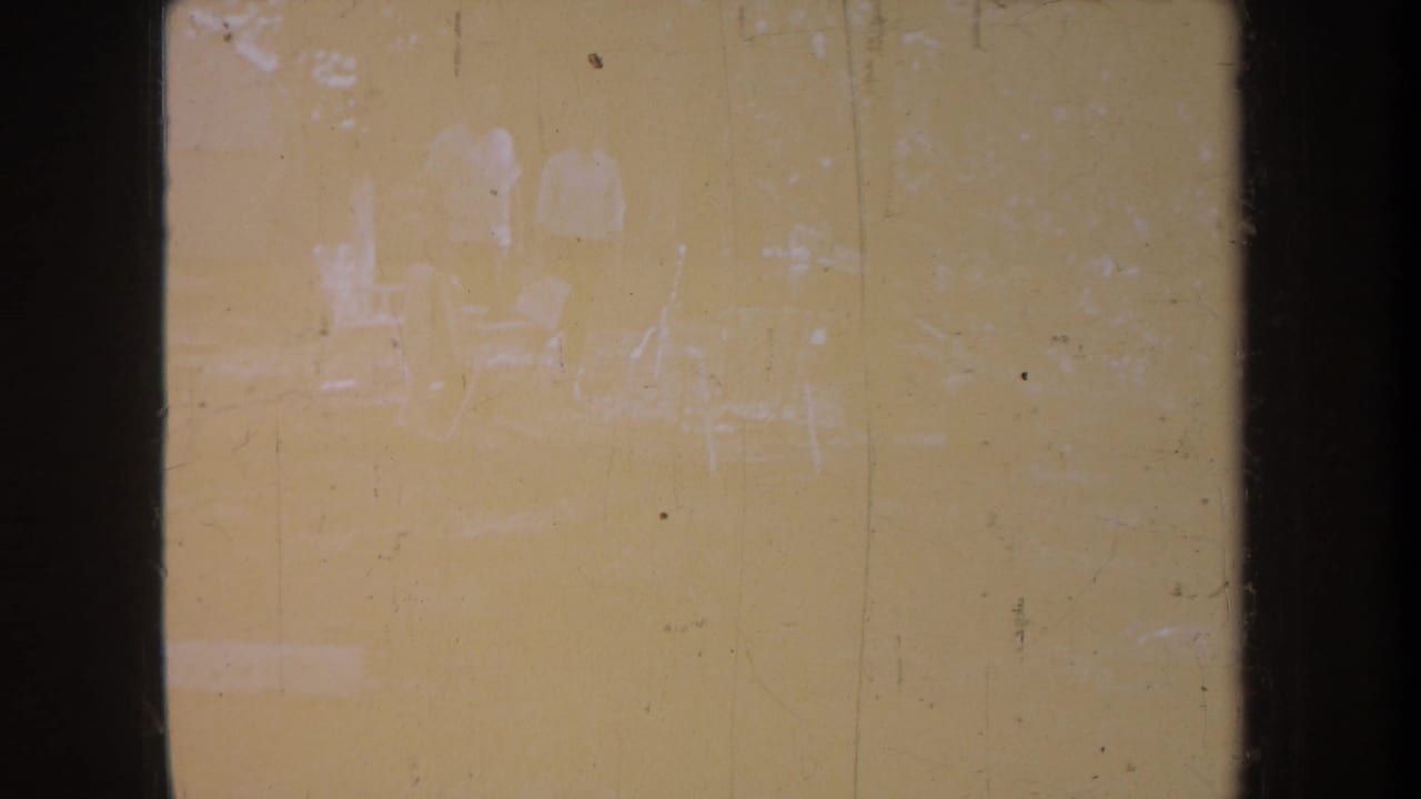 Faded yellow frame with indistinct figures, chairs, and trees near the top of the scene.