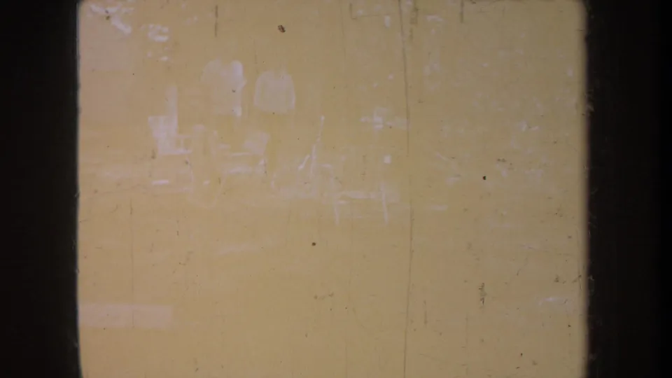 Soft, overexposed 1968 Michigan home-movie frame showing faint people and chairs in a wooded setting.