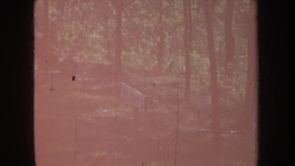 Faded 1968 Michigan 8mm frame showing a wooded trail area, trees, a railing or small bridge, and a faint sign.