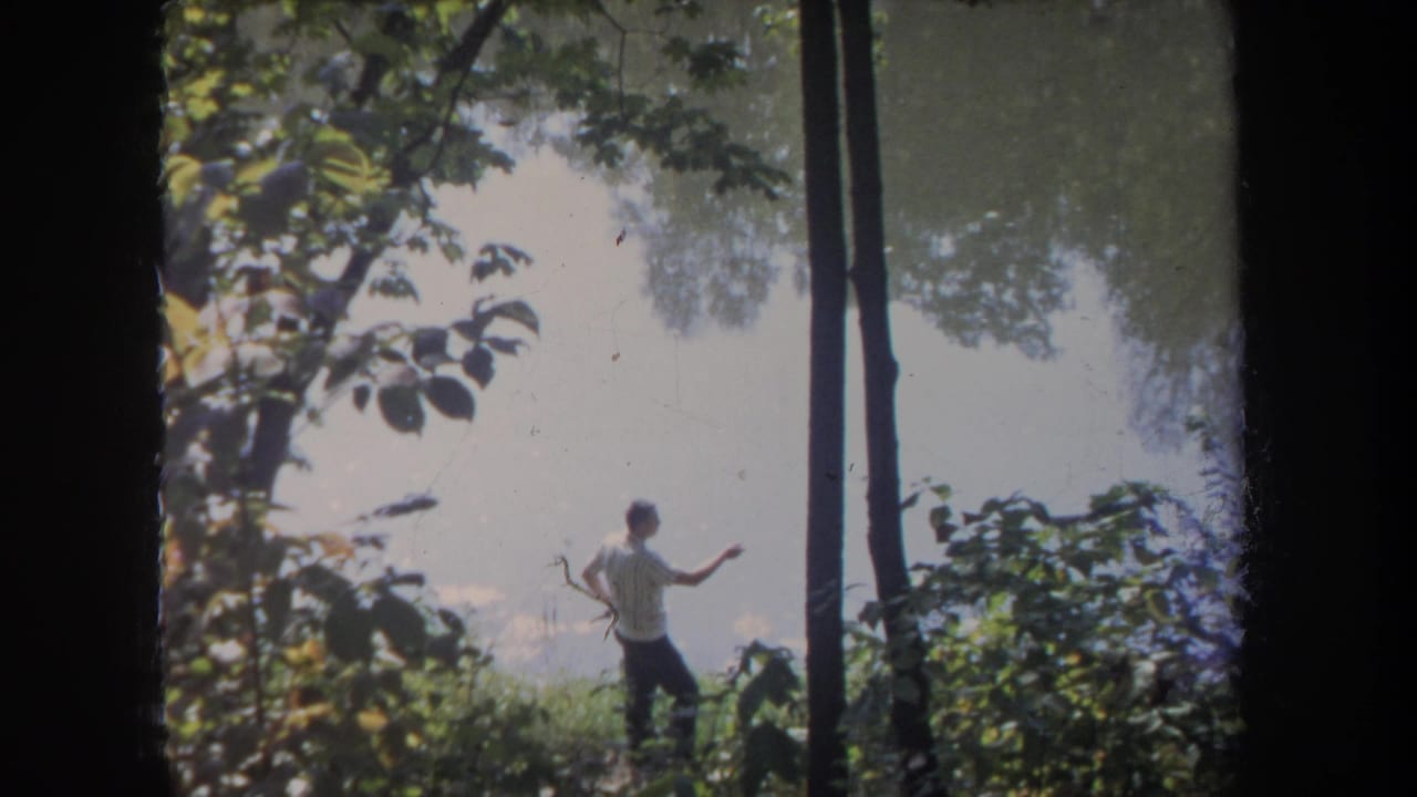 Man near the lake with one arm raised as if casting a fishing line.