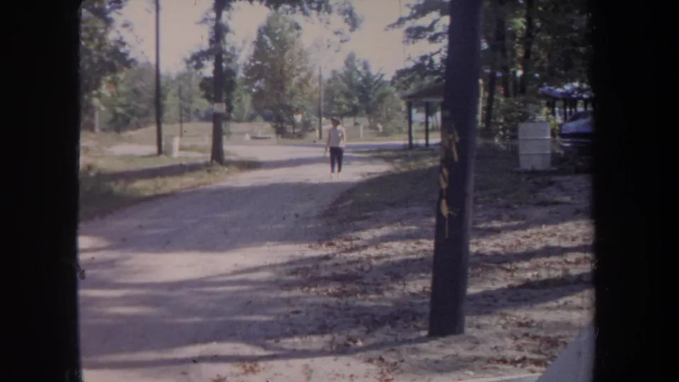 The final frame shows a man walking along a dirt road in a Michigan park-like setting in 1968 home-movie footage.