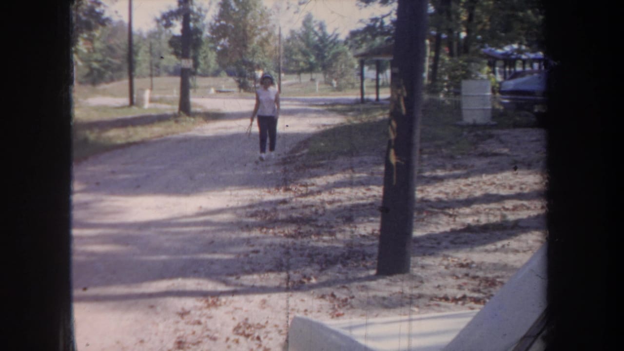 Woman farther along a tree-lined dirt road, partly framed by dark vertical edges.
