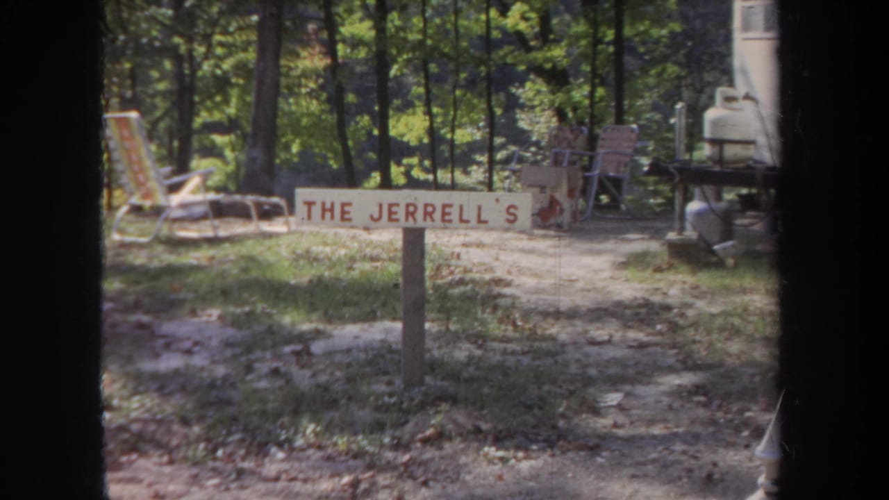 Wooded yard with a hand-painted The Jerrell's sign, chairs, and trailer equipment.