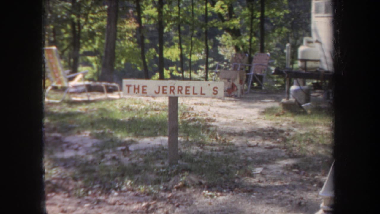 1968 Michigan frame of a family-name yard sign, folding chairs, trees, and trailer-side objects in soft 8mm color.