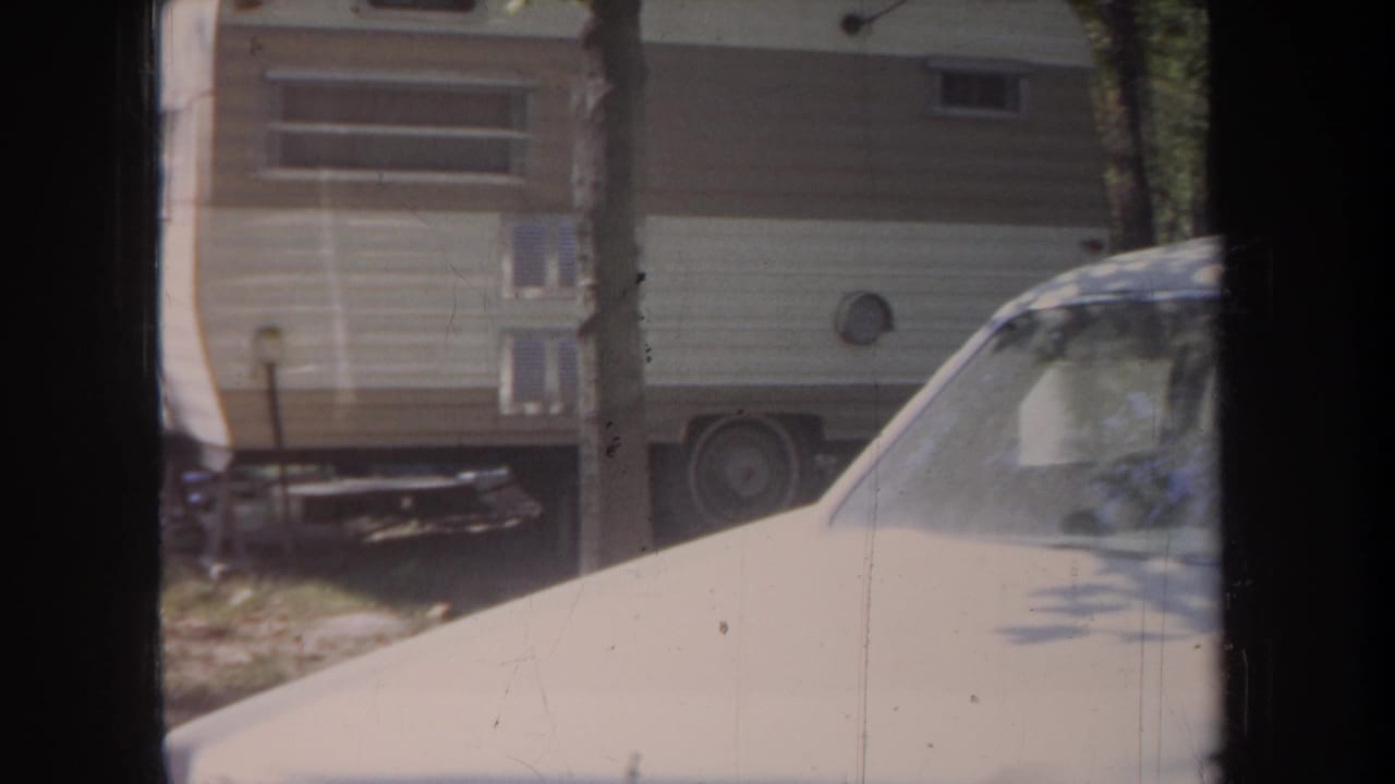 1968 Michigan 8mm frame showing a beige car in front of a cream-and-brown RV trailer among trees.