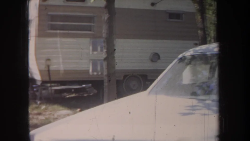 1968 Michigan 8mm frame showing a beige car in front of a cream-and-brown RV trailer among trees.