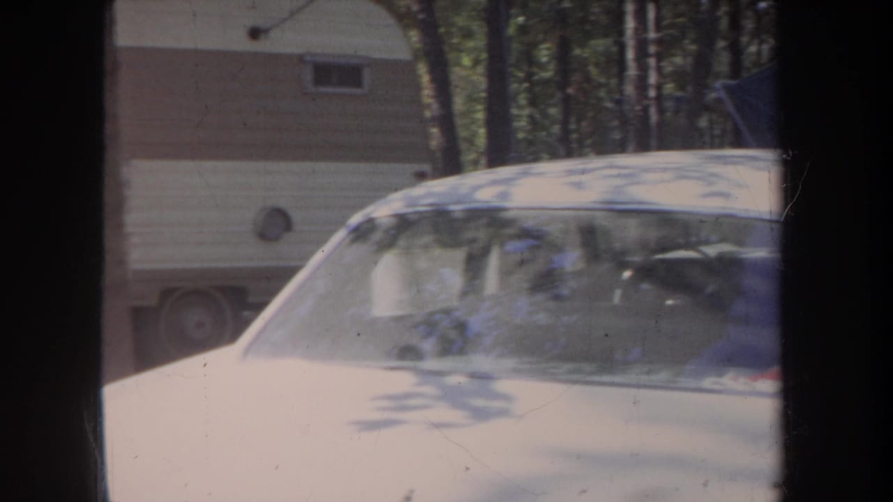 A beige car fills the foreground while a cream-and-brown trailer sits behind it at the Michigan campsite.