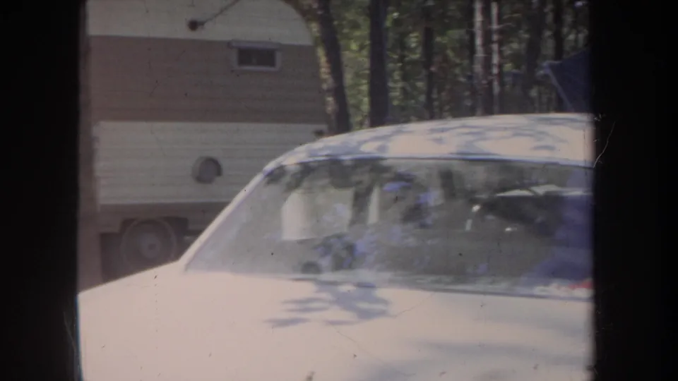 A beige car fills the foreground while a cream-and-brown trailer sits behind it at the Michigan campsite.