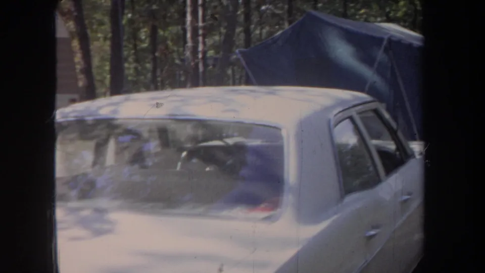 1968 Michigan camping frame with a beige sedan in the foreground and a blue canvas tent behind it.